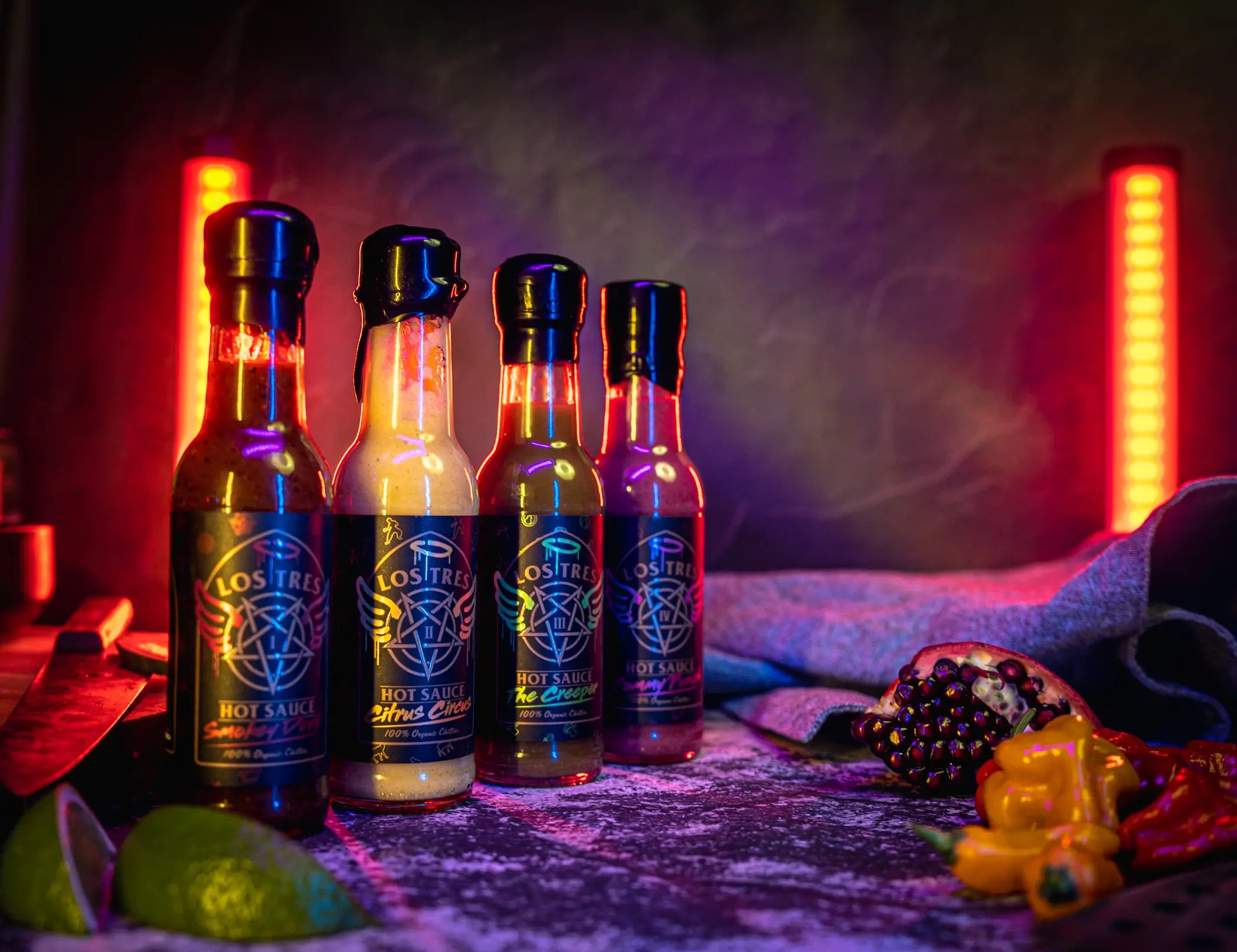 A long shot of the Los Tres sauce collection. This has four sauces in the shot with neon lights with chillies, lime and pomegranate